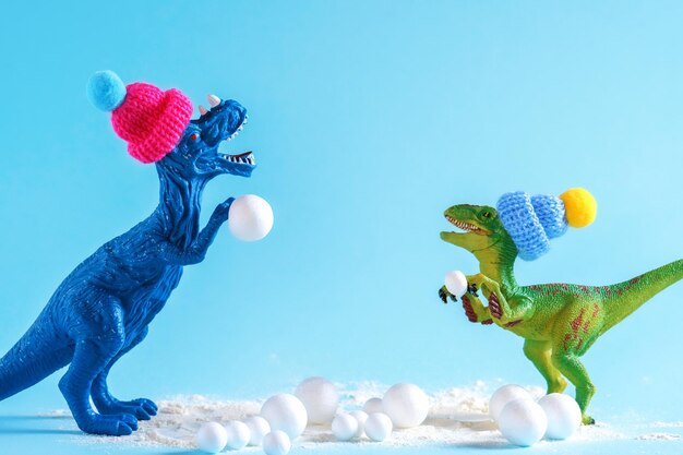 Foto dinossauros verdes e azuis bonitos com chapéus de tricô jogando bolas de neve feliz cartão de férias de inverno