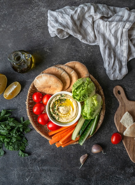 Dip de hummus tradicional casero hecho con verduras frescas, pita y hierbas en bandeja. Vista superior.