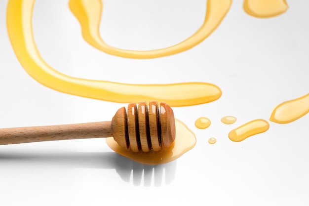 Dipper für Honig liegt in flüssigem Honig auf weißem Hintergrund