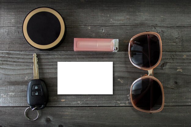 Foto directamente por encima de la toma de llave de coche cosmético lápiz labial gafas de sol y papel en madera oscura