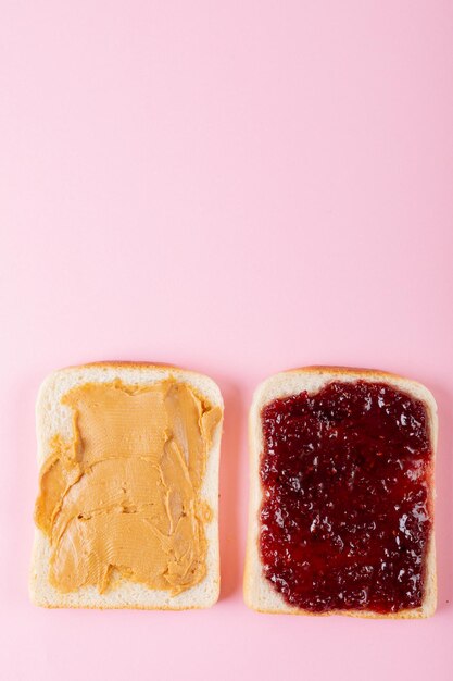 Foto directamente encima de la toma de un sándwich de mantequilla de maní y jalea de cara abierta sobre fondo rosa con espacio para copiar