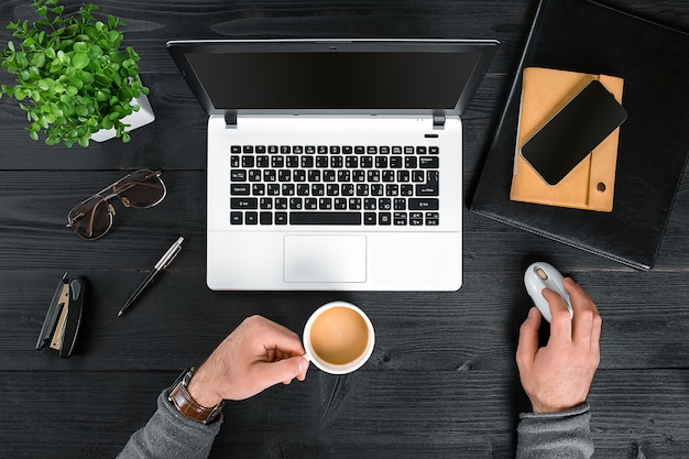 Directamente encima de la vista de manos humanas escribiendo en la computadora portátil. Ordenador portátil, tableta digital, agenda, taza de café y planta en maceta en la mesa de trabajo. Hombre trabajando desde casa.