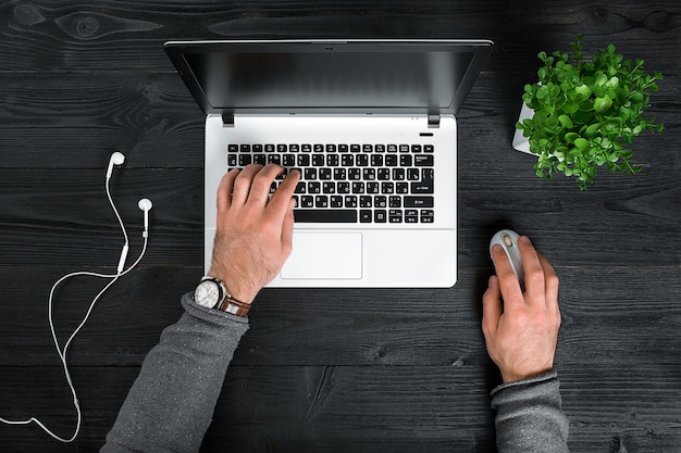 Directamente encima de la vista de manos humanas escribiendo en la computadora portátil. Ordenador portátil, tableta digital y planta en maceta en la mesa de trabajo. Hombre trabajando desde casa.