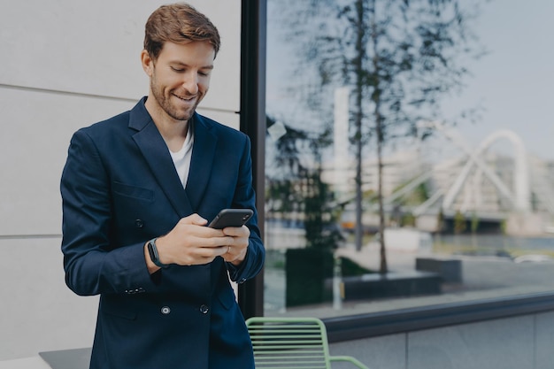 El director o ceo masculino guapo complacido sostiene el teléfono móvil espera una llamada