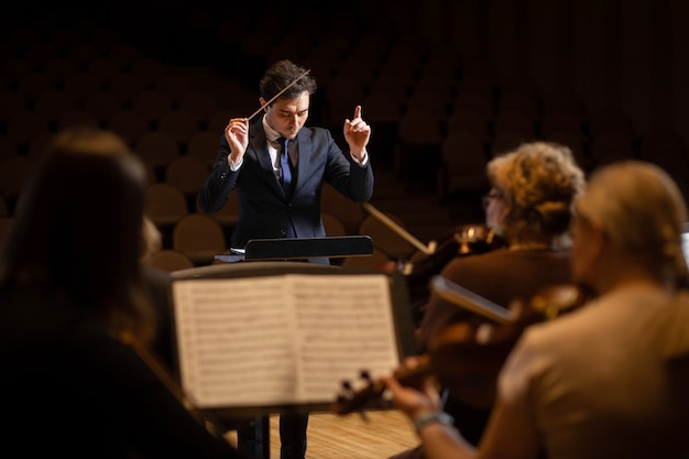 Foto director de orquesta sinfónica con artistas en el fondo de la sala de conciertos