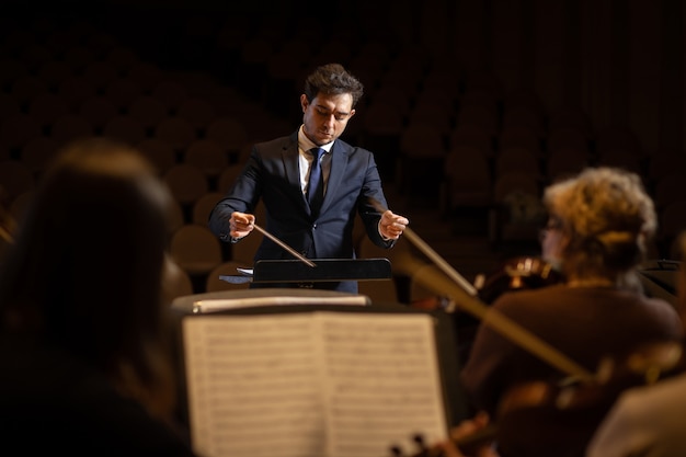 Director de orquesta sinfónica con artistas en el fondo de la sala de conciertos