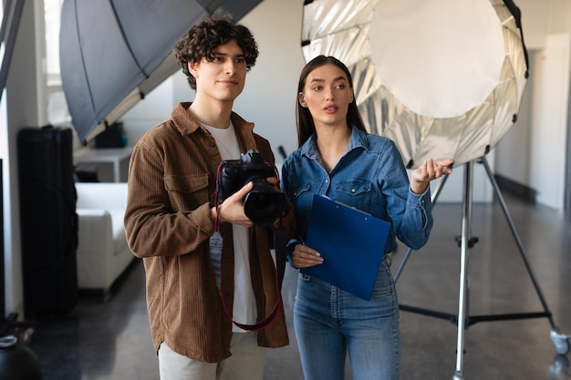 Directora de arte femenina explicando a la fotógrafa sobre la sesión de fotos de pie cerca del espacio libre de equipos de iluminación modernos