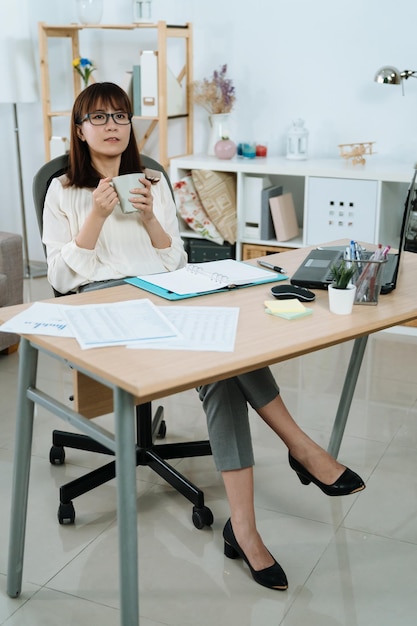 la directora ejecutiva mira a lo lejos y reflexiona sobre su futuro en su oficina. una mujer de aspecto inteligente sostiene una taza de café y piensa en su carrera.