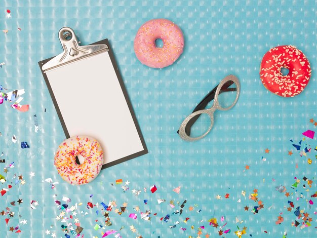 Foto direkt oberhalb der aufnahme von clipboard mit donuts und farbenfrohen konfetti auf dem tisch