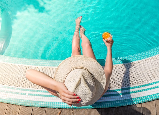 Direkt über der Aufnahme einer Frau mit einem Getränk, die am Pool sitzt