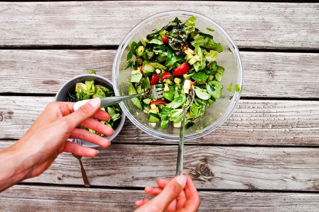 Foto direkt über der hand, die salat in einer schüssel auf dem tisch mischt