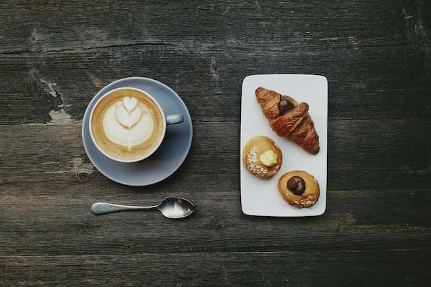 Direkt über der Kaffeetasse und dem Croissant mit Gebäck auf dem Holztisch