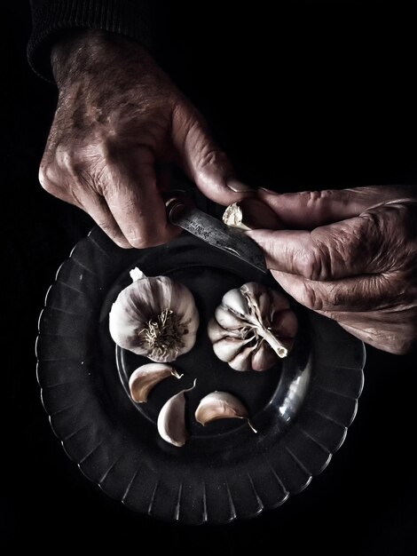 Direkt über einem Mann, der Knoblauch vor schwarzem Hintergrund schält