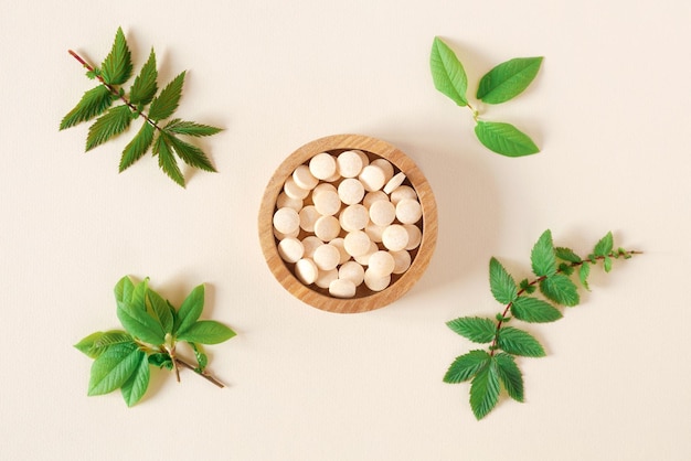 Direkt über Pillen und grünen Blättern Tabletten in Holzschale auf beigefarbenem Hintergrund in neutralen Farben