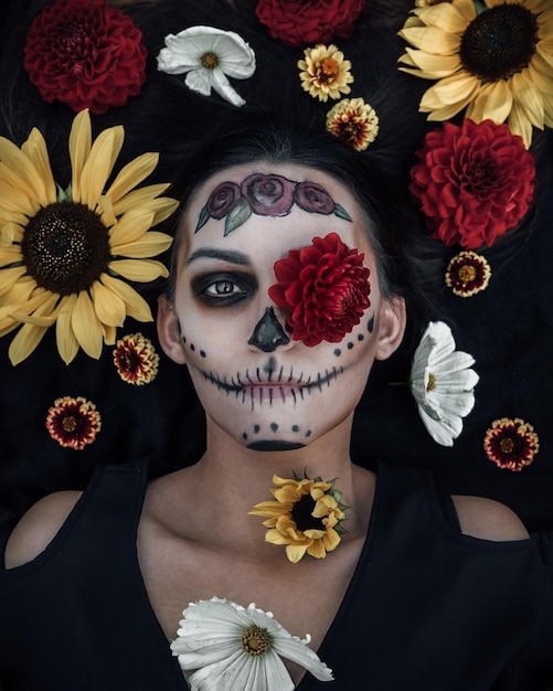 Direkt über Porträt einer Frau mit Halloween-Make-up, die inmitten von Blumen liegt