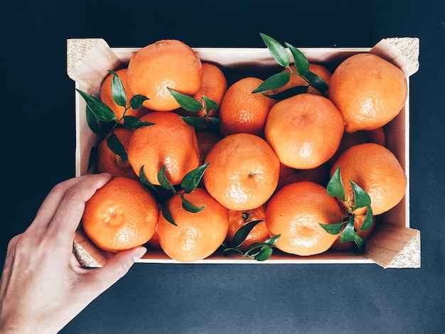 Diretamente acima da foto da mão cortada tomando laranja de uma caixa de madeira