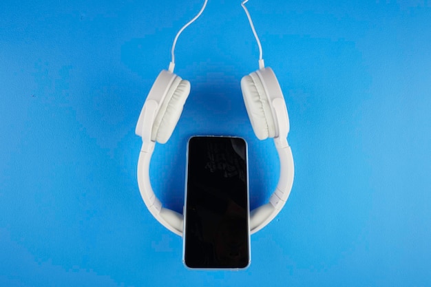 Diretamente acima da foto de um telefone inteligente com fones de ouvido sobre um fundo azul