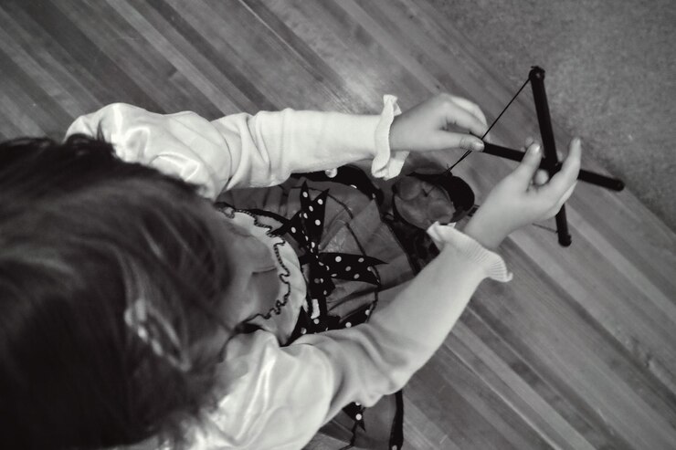 Foto diretamente acima da foto de uma menina brincando com uma marioneta enquanto estava de pé no chão de madeira