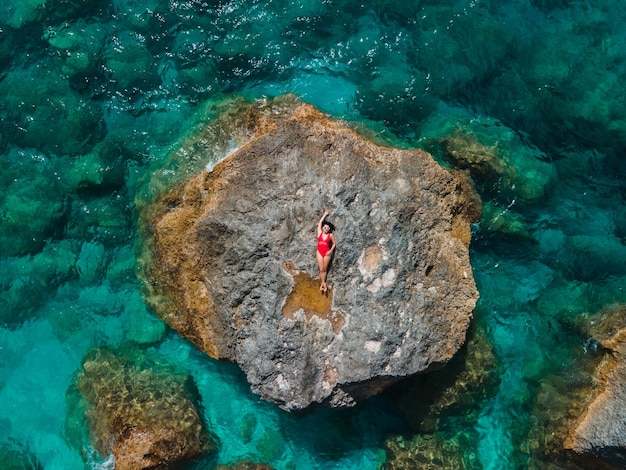 Diretamente acima da mulher de maiô vermelho na rocha cercada pelas férias do mar na grécia