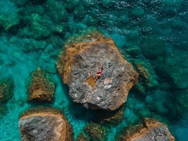 Diretamente acima da mulher em um maiô vermelho na rocha cercada pelo mar, férias na Grécia