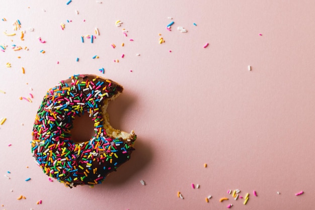 Diretamente acima da vista da falta de um donut de chocolate com sprinklers espalhados em fundo rosa