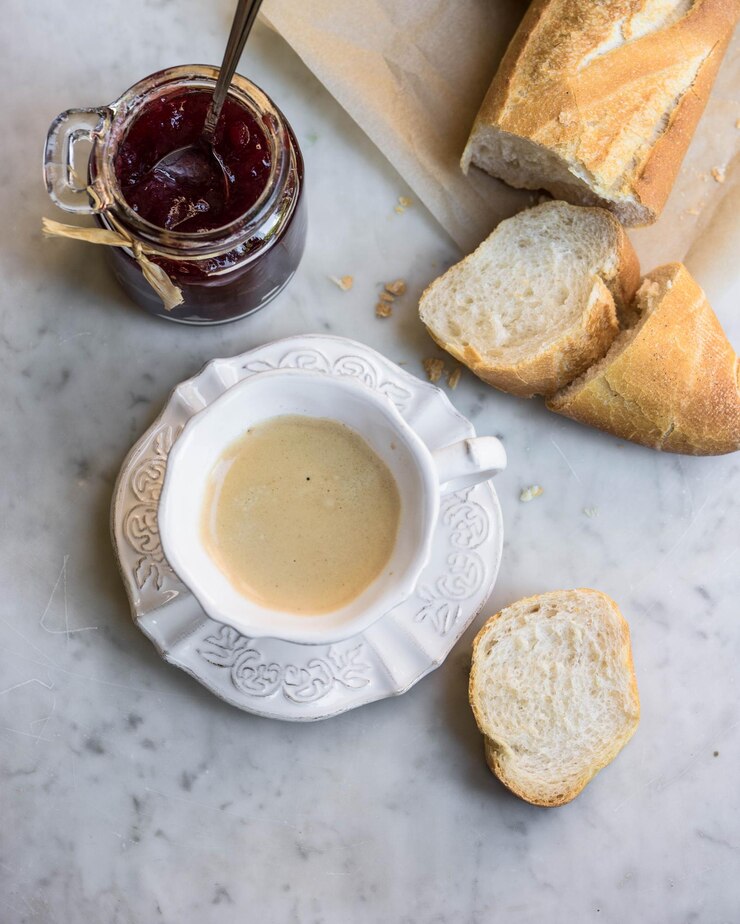Foto diretamente acima de um copo de café com geleia de morango e baguete na mesa