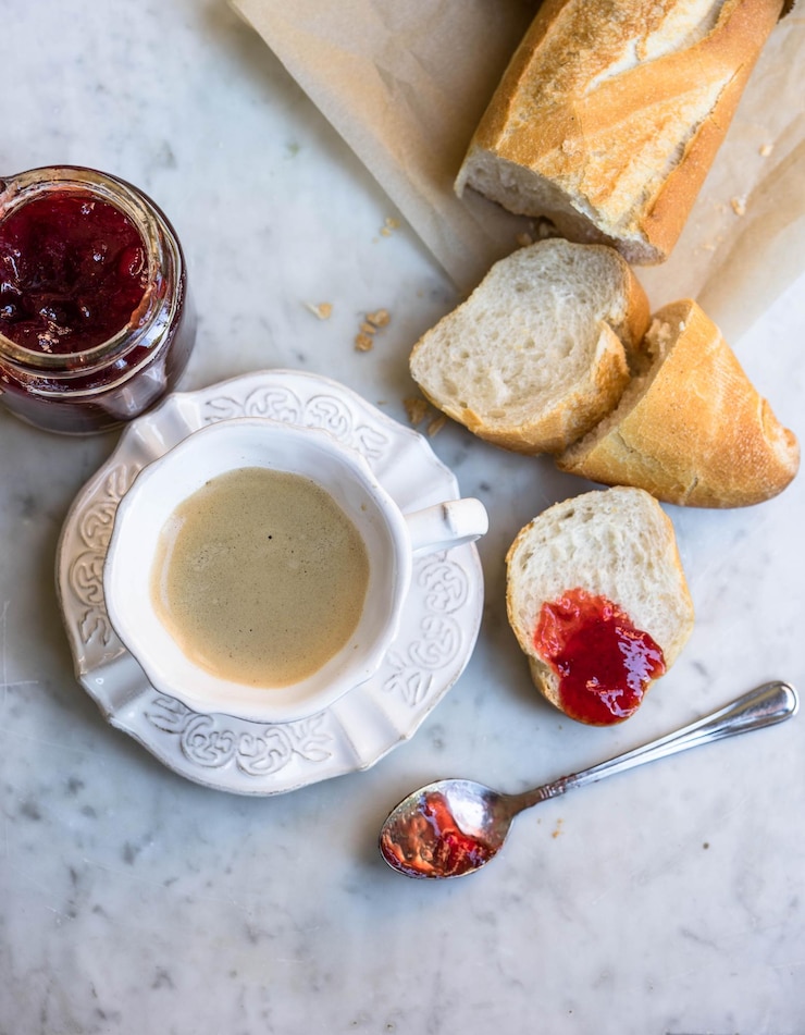 Foto diretamente acima de um copo de café com geleia de morango e baguete na mesa