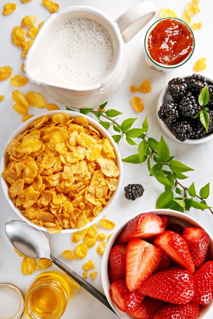 Foto diretamente acima do pequeno-almoço com flocos de milho e frutas por jarro de leite