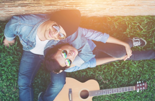 Diretamente acima do retrato de um casal feliz sentado ao lado da guitarra em um campo gramado