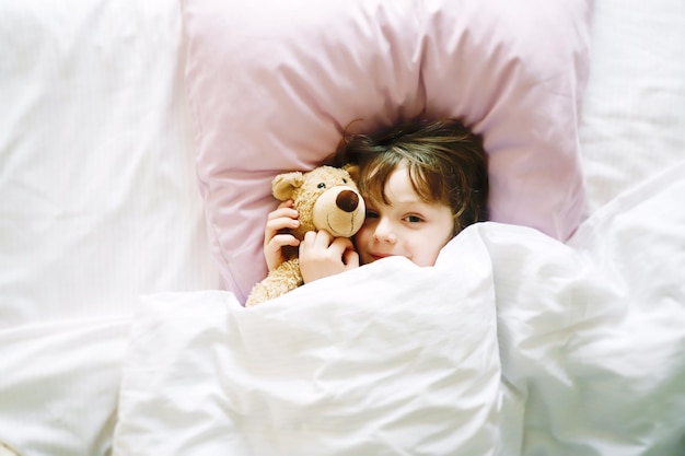 Diretamente acima do retrato de um menino bonito com um ursinho de pelúcia deitado na cama em casa