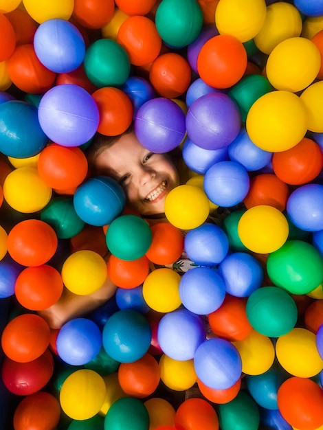 Foto diretamente acima do retrato de um menino brincalhão sorridente em meio a uma piscina de bolas colorida