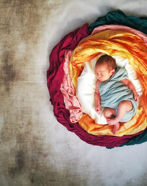 Foto diretamente acima, uma foto de bebês dormindo em meio a tecidos coloridos.
