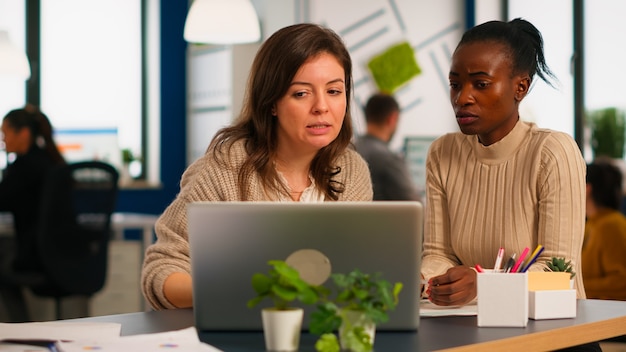 Diretor da empresa explicando para a mulher negra os resultados do projeto, fazendo alterações, trabalhando em frente ao laptop, sentado à mesa no escritório da empresa iniciante. Conceito de trabalho em equipe e cooperação