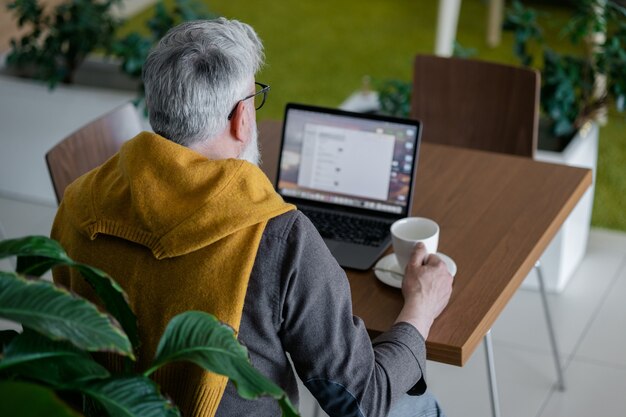 Diretor ou gerente sênior bonito de cabelos grisalhos trabalhando com um laptop e conversando online