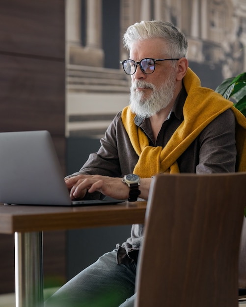 Diretor ou gerente sênior bonito de cabelos grisalhos trabalhando com um laptop e conversando online