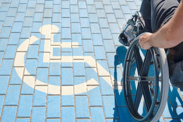 Un discapacitado irreconocible en silla de ruedas pasando por encima de un cartel de discapacitado pintado en el suelo