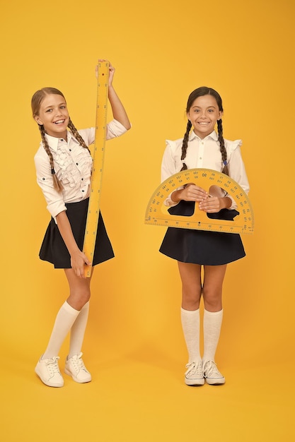 Disciplinas de tallo de matemáticas felices regreso a la escuela Matemáticas y geometría Niños en uniforme en la pared amarilla amistad y hermandad niñas pequeñas felices estudian matemáticas los estudiantes usan regla de transportador