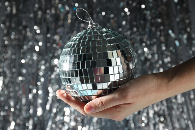 Foto disco-ball in der hand mit feierlichen silbernen bändern auf dem hintergrund