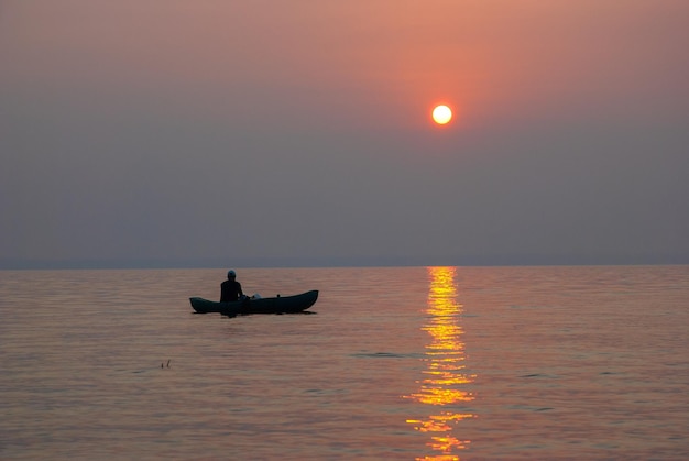 Disco brillante del sol al atardecer y un camino naranja en el lago con un pescador en un bote