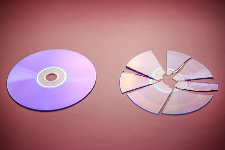 Foto disco compacto quebrado dividido em partes e um disco compacto inteiro em um fundo redburgundy