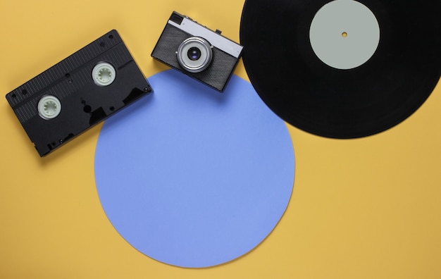 Disco de vinil retrô, videocassete, câmera de filme sobre fundo de cor amarela com um círculo azul. Vista do topo