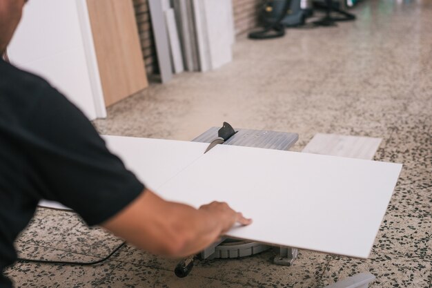 Disco eléctrico cortando una plancha blanca sostenida por un hombre adulto en un taller.