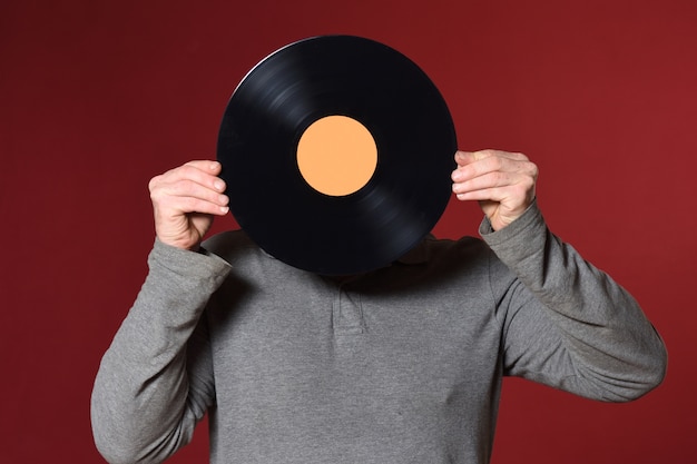 Foto disco de música cubre su rostro sobre fondo rojo.