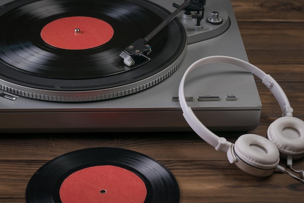 Un disco de vinilo y auriculares blancos están al lado del reproductor en una mesa de madera