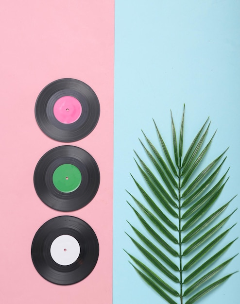 Discos de vinil e folhas verdes de palma em fundo rosa azul Conceito de música Composição tropical Vista superior Flat lay