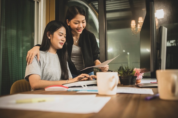 Discusión independiente de dos mujeres asiáticas más jóvenes al trabajo en la computadora de la oficina