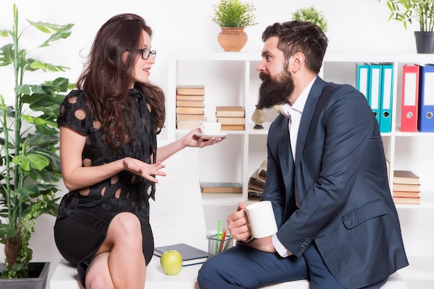 Discusión sobre una taza de té Pareja profesional que participa en una discusión de negocios durante el descanso laboral Discusión de empresarios relajándose y comunicándose en el escritorio Discusión sobre negocios