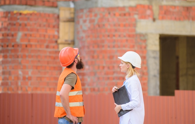 Discuta o projeto de progresso. Conceito de indústria de construção. Engenheira e construtor barbudo brutal discutem o andamento da construção. Gerenciamento de projetos de construção. Projeto de construção industrial.