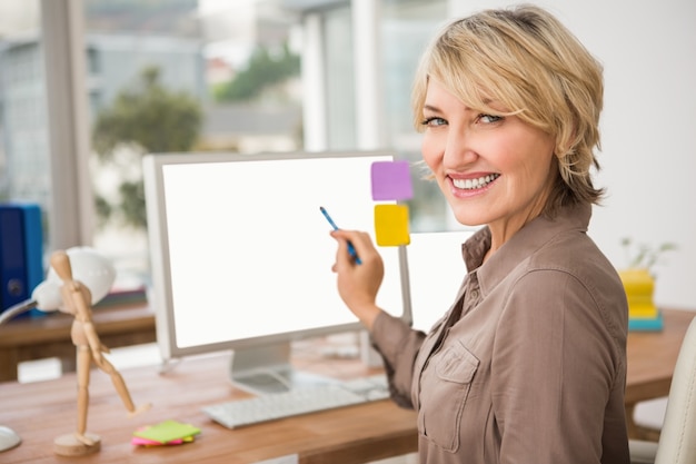 Diseñador casual sonriente que señala la pantalla de ordenador en blanco