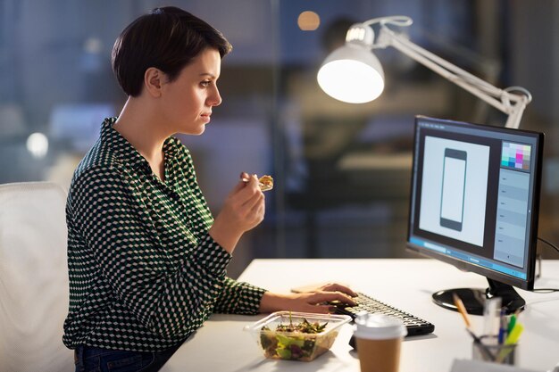 Foto diseñador comiendo y trabajando en la oficina nocturna